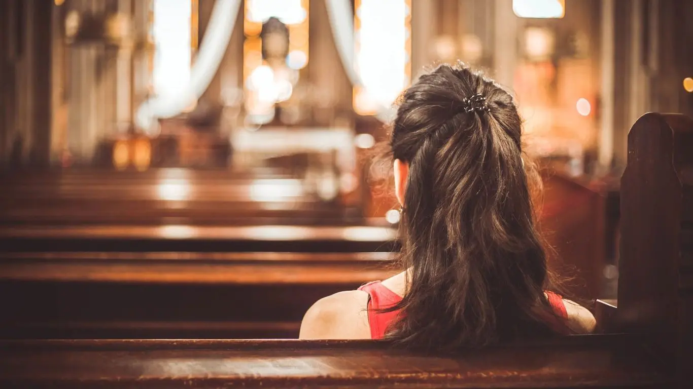 A woman sitting in the middle of a church pews.