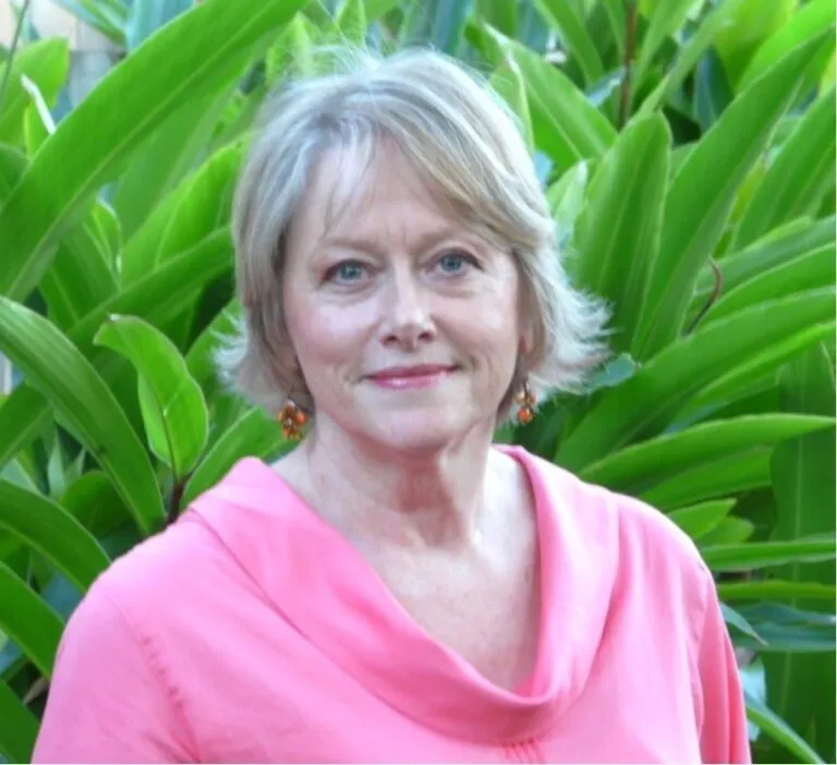 A woman in pink shirt standing next to green plants.