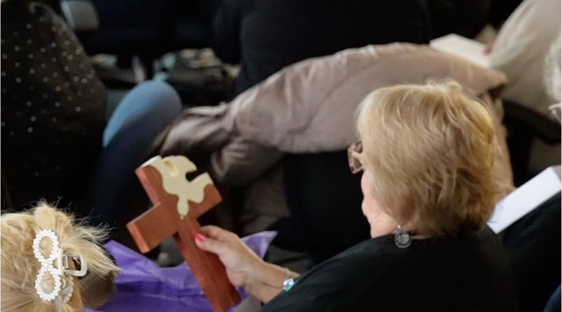 A woman holding a wooden cross sitting on the ground.