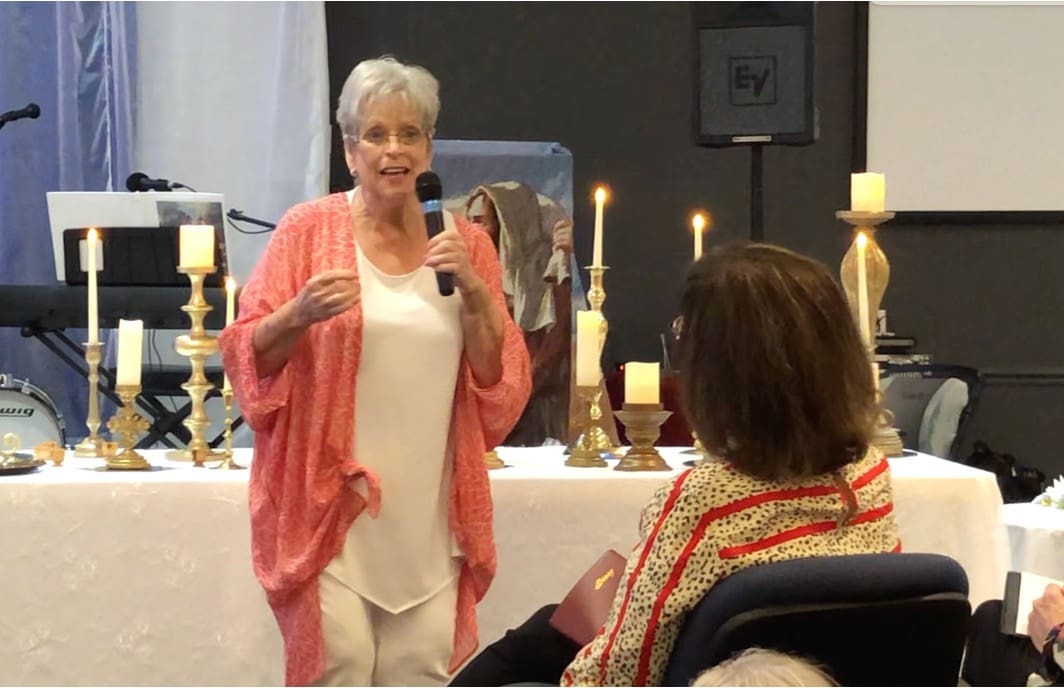 A woman is speaking to people in front of candles.