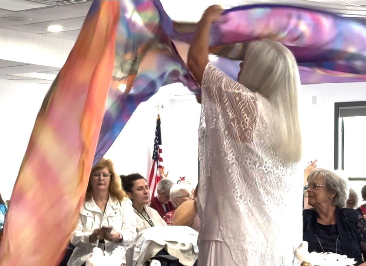 A woman in white dress holding onto a colorful scarf.