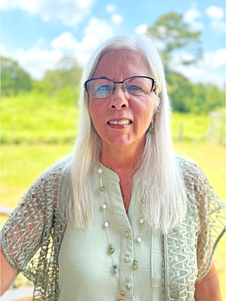 A woman with white hair wearing glasses and smiling.