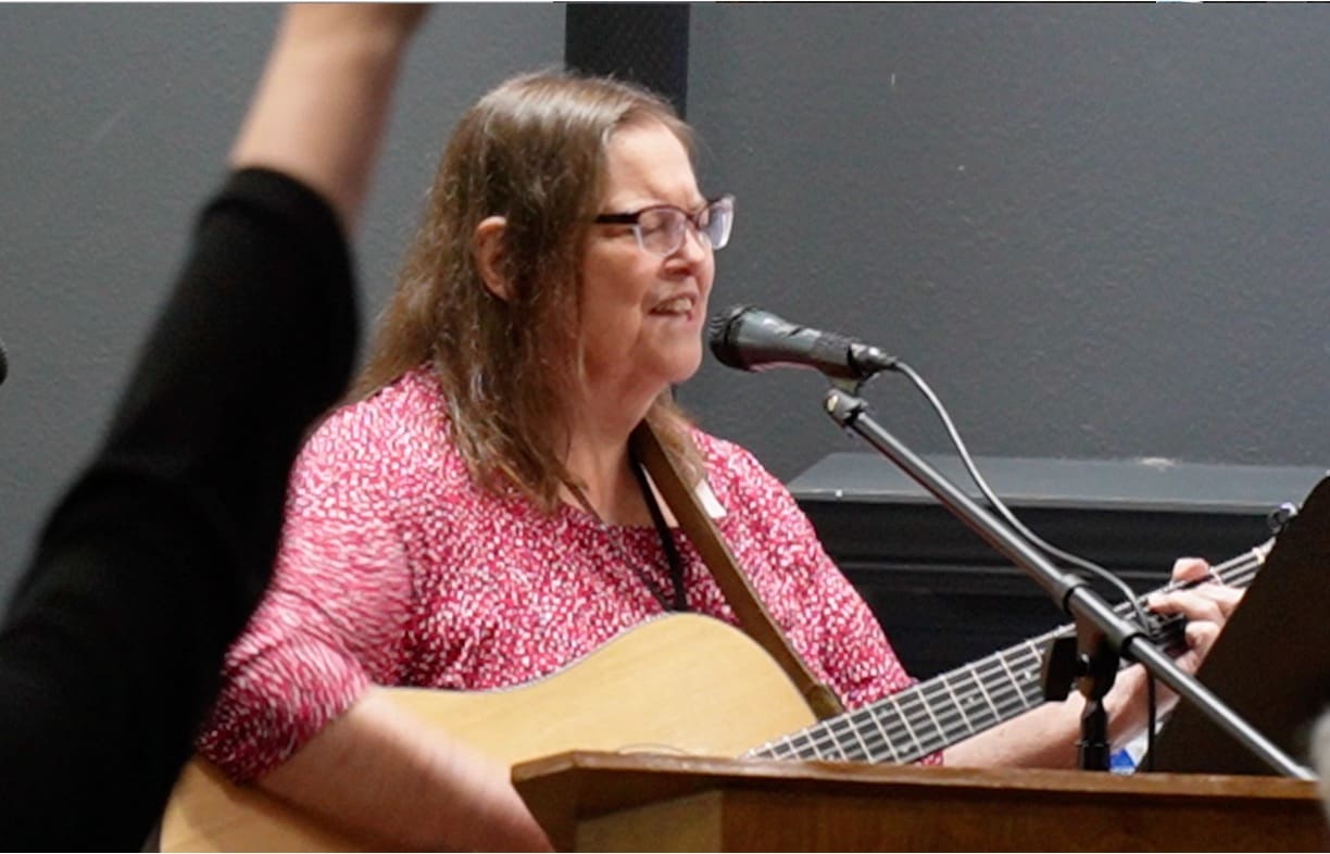 A woman in glasses is playing the guitar