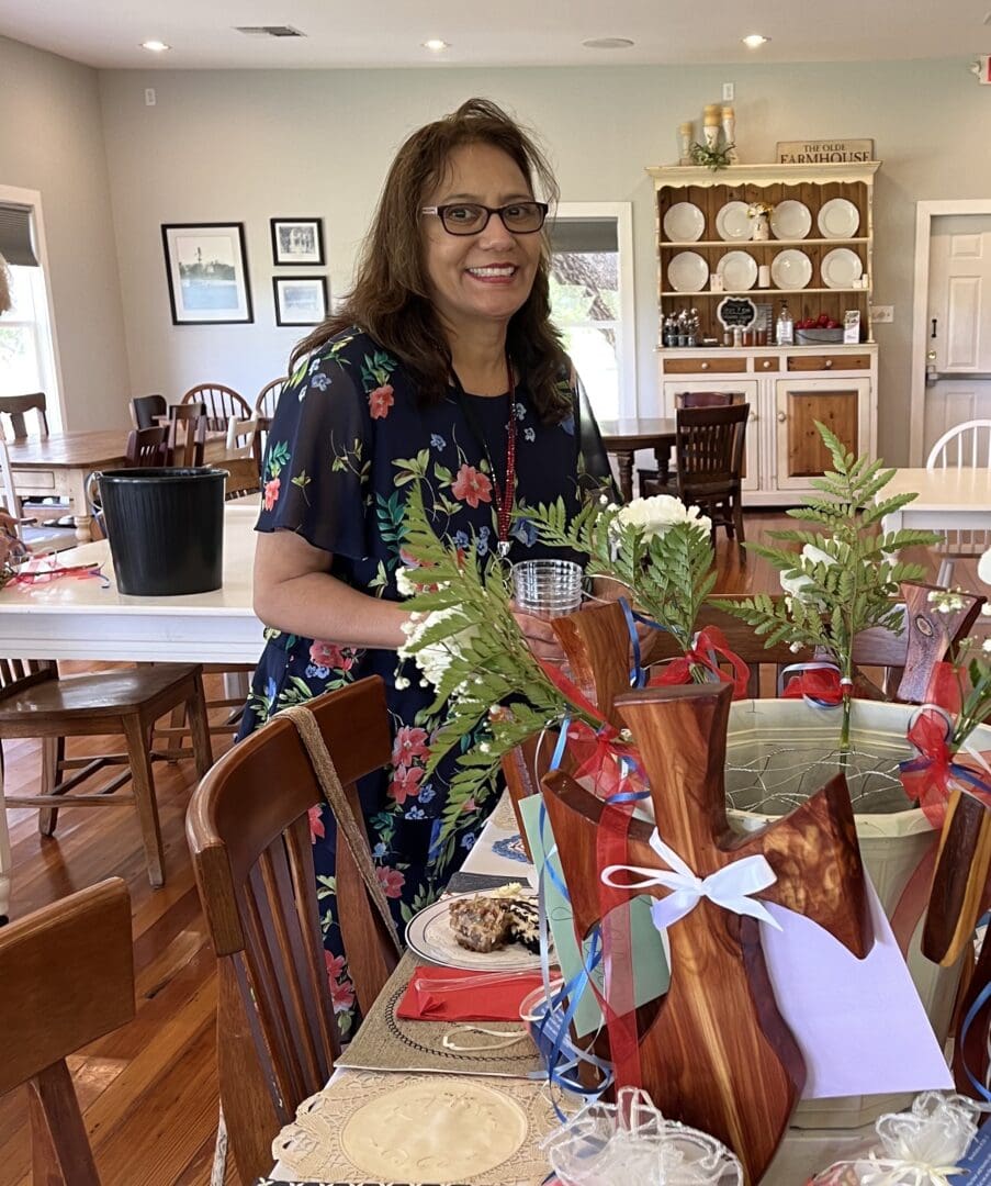 A woman standing at the table with flowers in it.