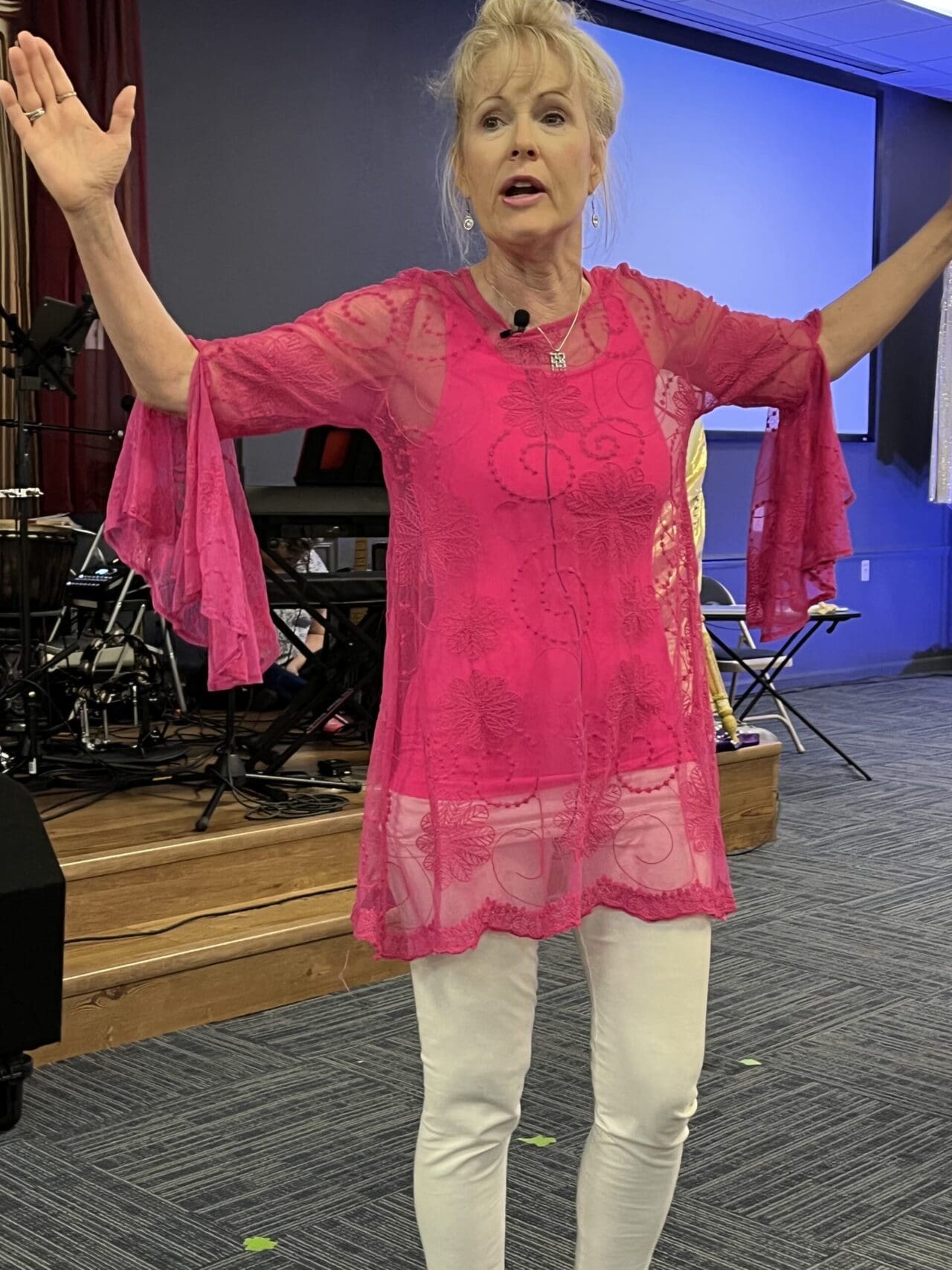 A woman in pink shirt and white pants standing on stage.