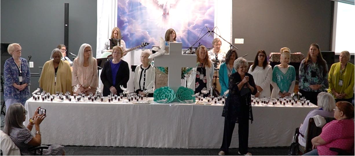 A group of women sitting at a table with a cross.