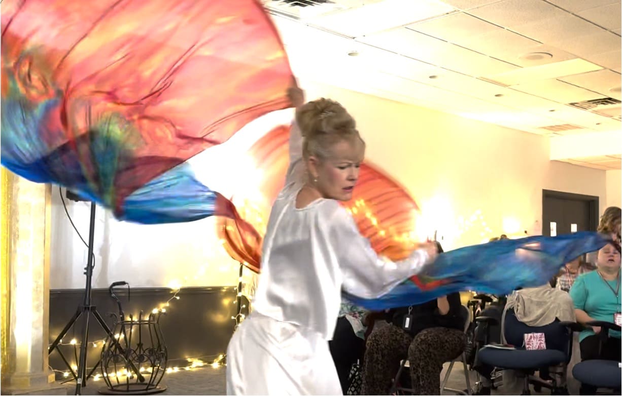 A woman in white shirt holding up a colorful flag.