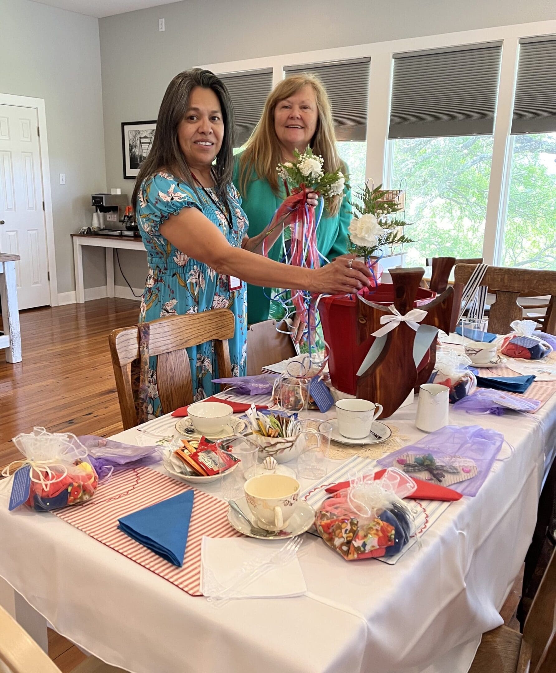 Two women standing at a table with tea cups and plates.