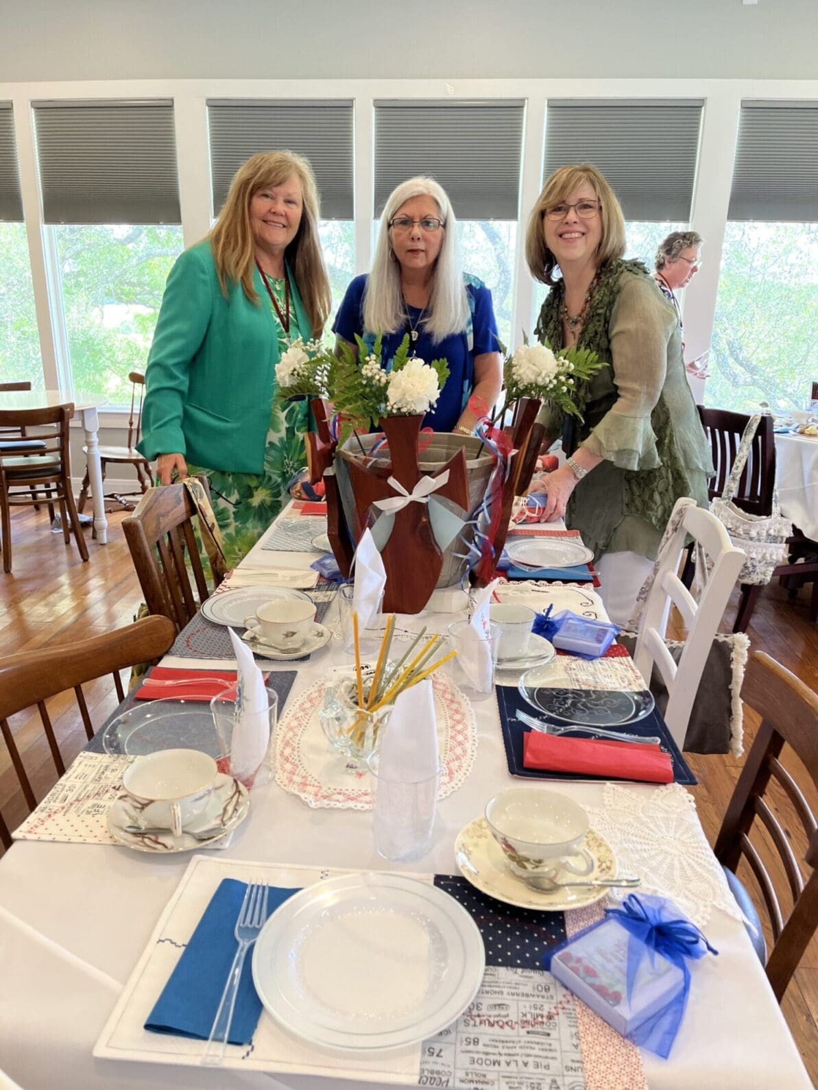 Three women standing at a long table with plates and flowers.