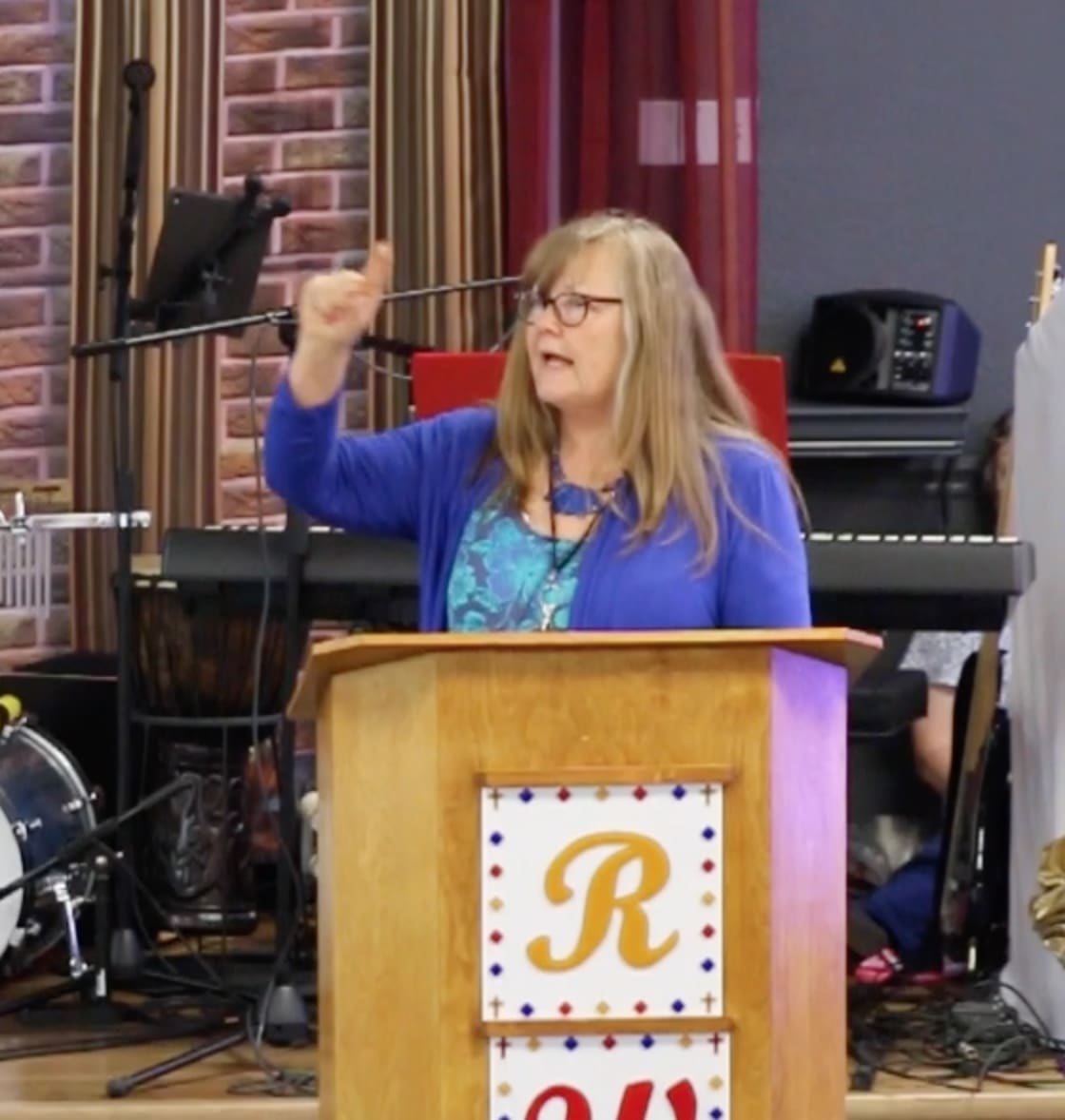 A woman is holding up her hand while standing at the podium.