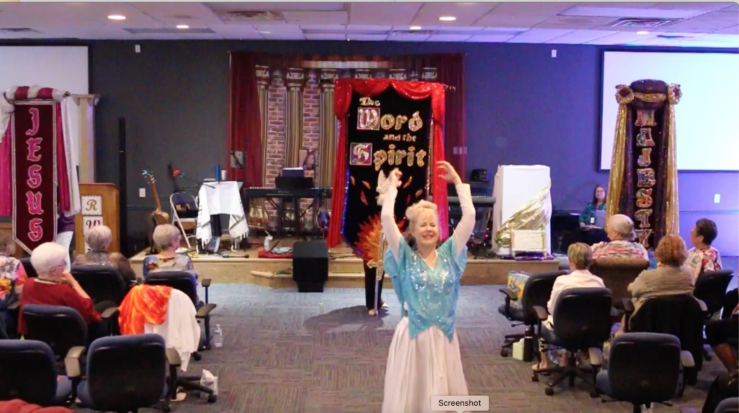 A woman in blue shirt and white skirt holding her hands up.