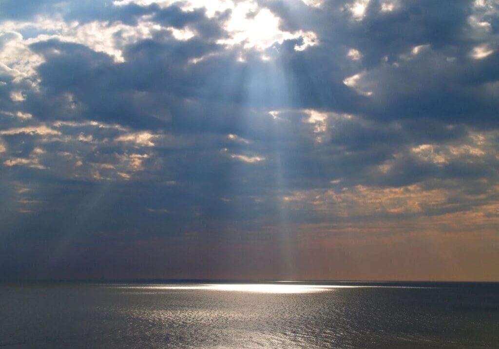 A sun beam shining through the clouds over an ocean.