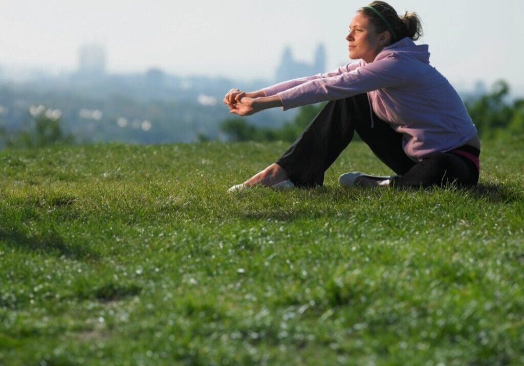 A woman sitting on the grass in front of some trees