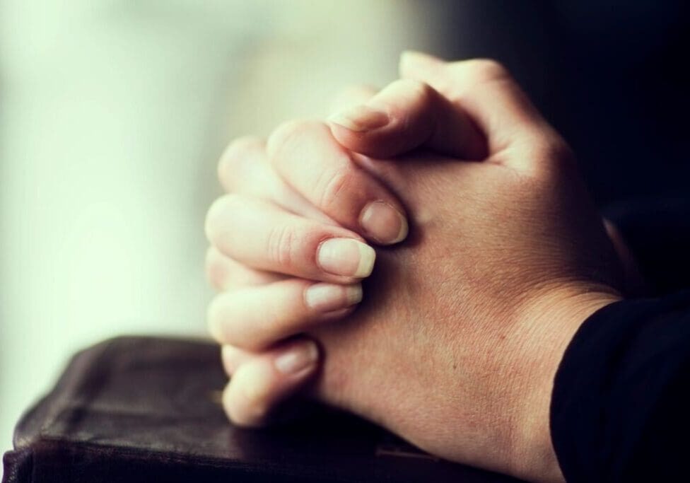 A person 's hands folded in prayer on top of a table.