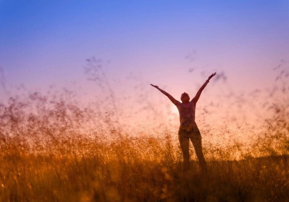 A woman standing in the grass with her arms outstretched.