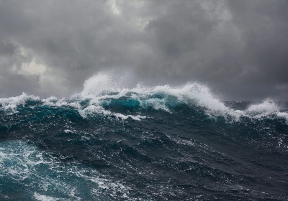 A large wave is in the ocean under a cloudy sky.