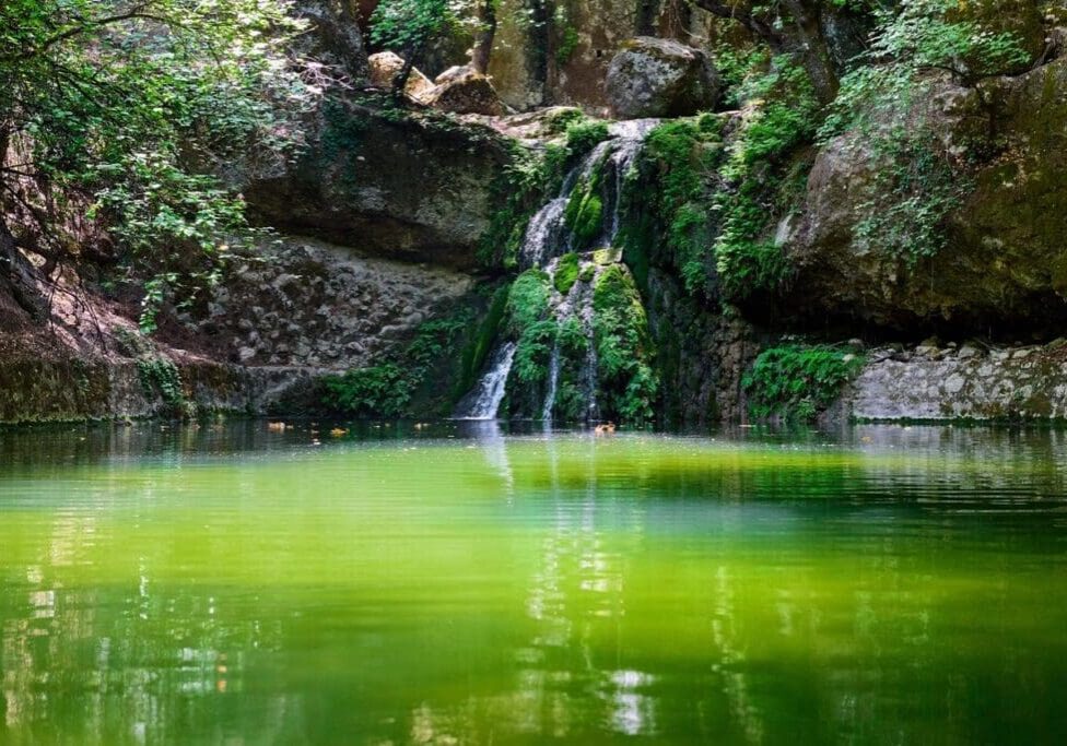 A waterfall with green water and rocks in the background.