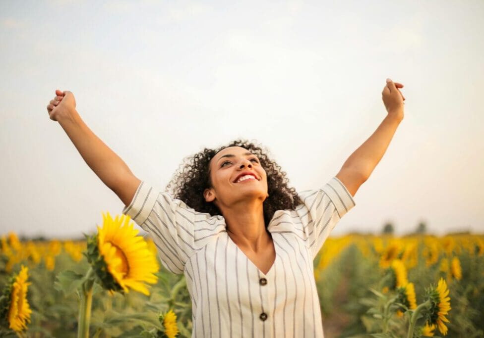 A woman standing in the middle of a field with her arms raised.